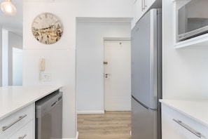A modern kitchen with white cabinetry, a stainless steel refrigerator, and a wall-mounted clock.