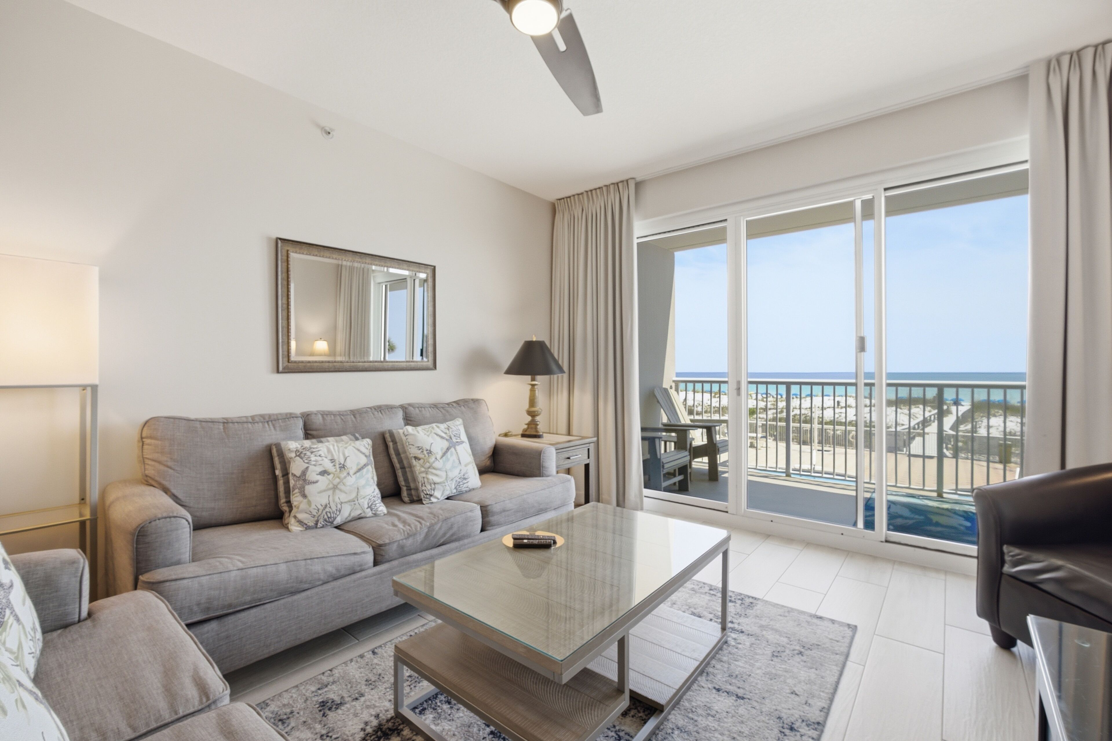 Un salon moderne avec un canapé, une table basse et une vue sur la plage grâce à de grandes portes-fenêtres coulissantes.