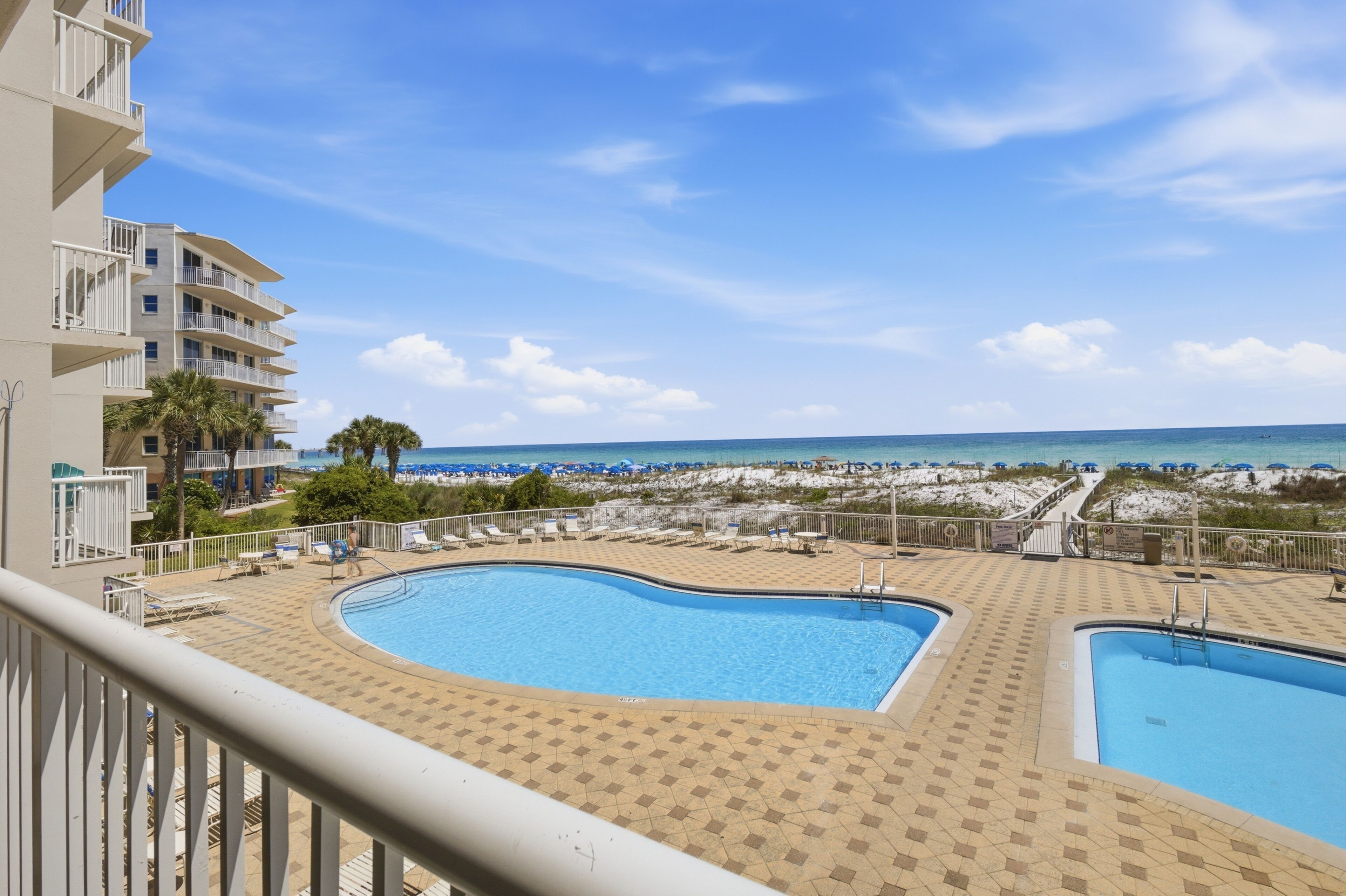 A pool area with two pools, a beach view, and a building with balconies.