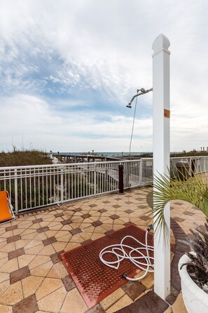 A terrace with a view of the beach, a white railing, and a potted plant.