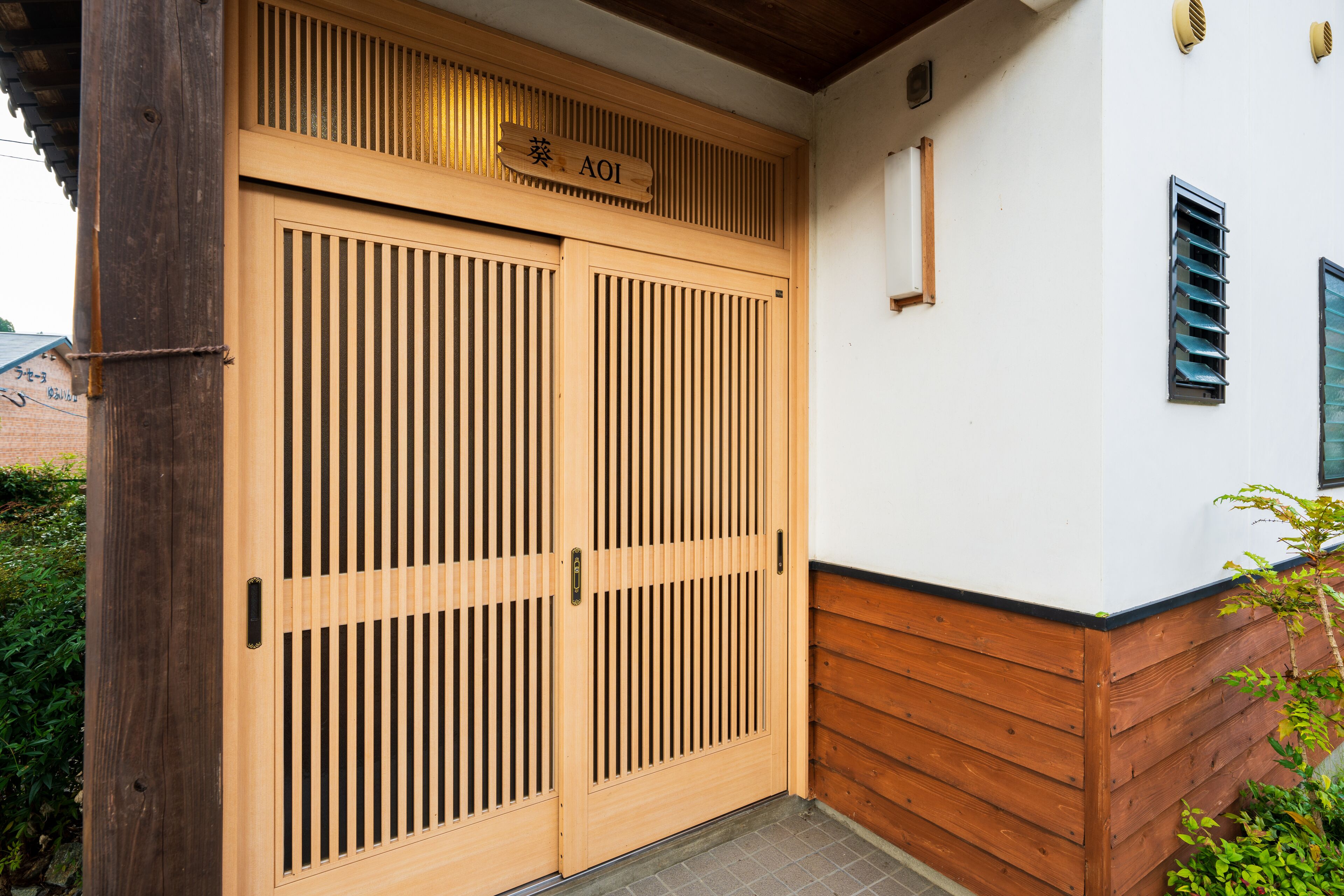 A wooden gate with a sign above it, a white building with a wooden baseboard, and a small window with shutters.