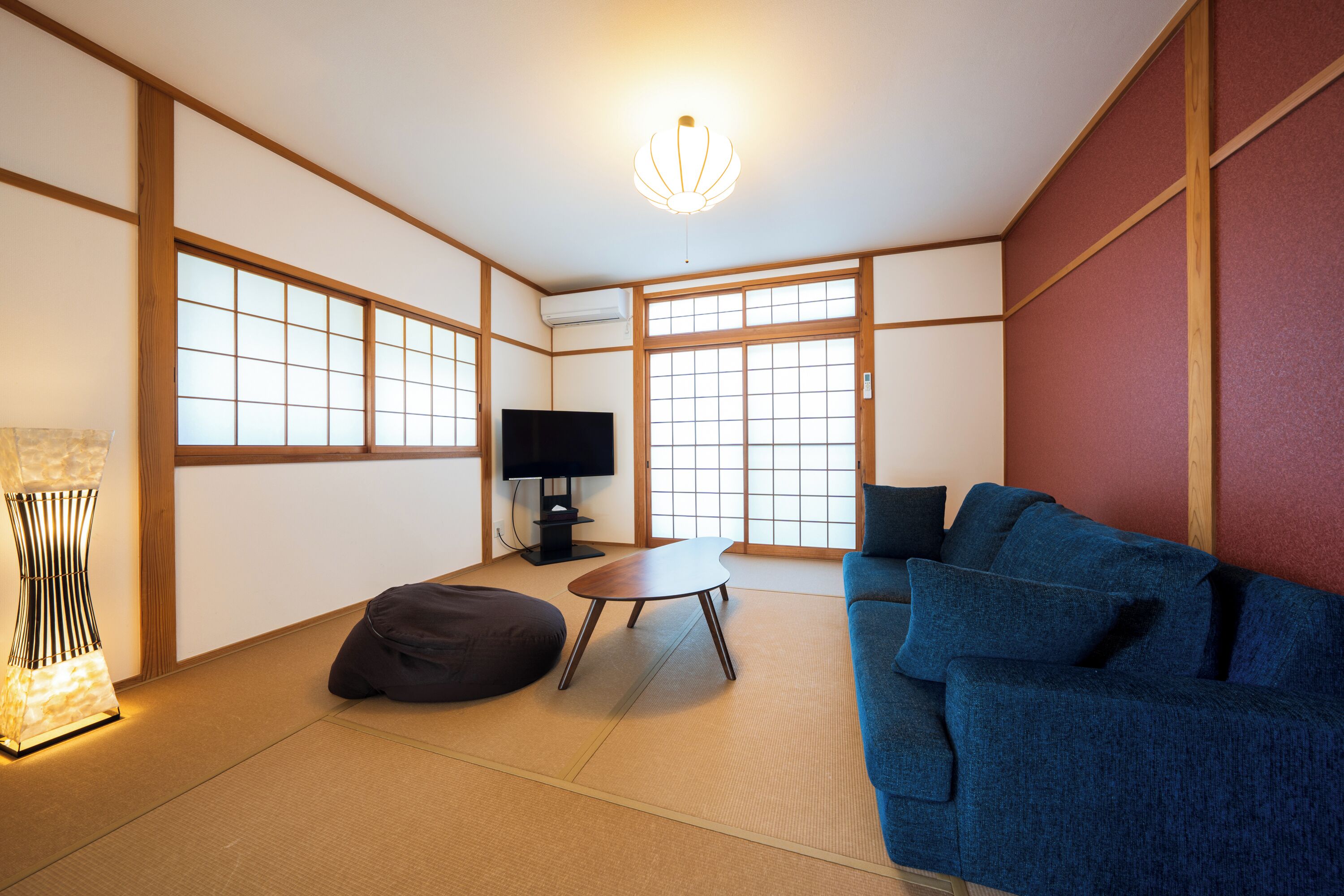 A traditional Japanese-style room with tatami flooring, a blue sofa, a small table, and a television.