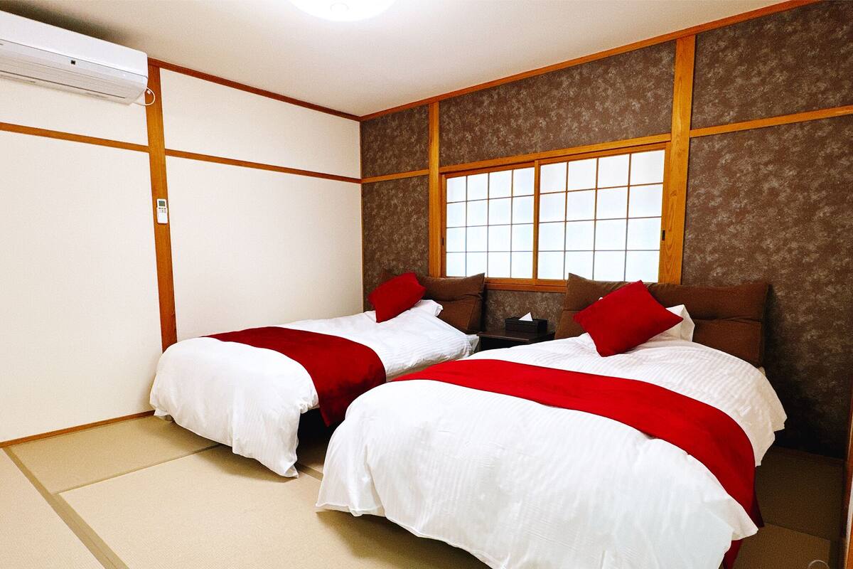 Une chambre d’hôtel avec deux lits, une fenêtre et un mur de style japonais traditionnel.