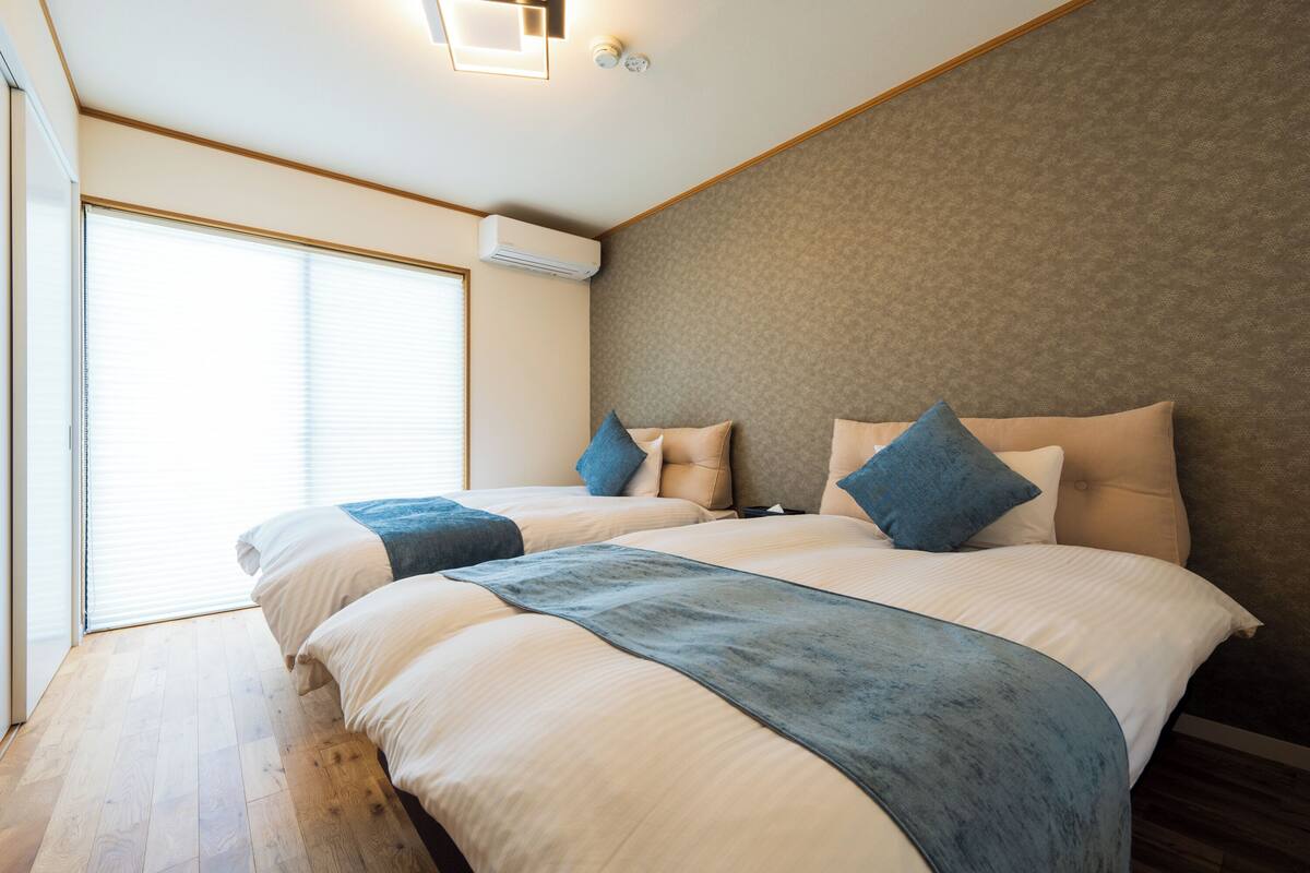 Une chambre d’hôtel moderne avec un grand lit, une fenêtre équipée de stores et un climatiseur fixé au mur.