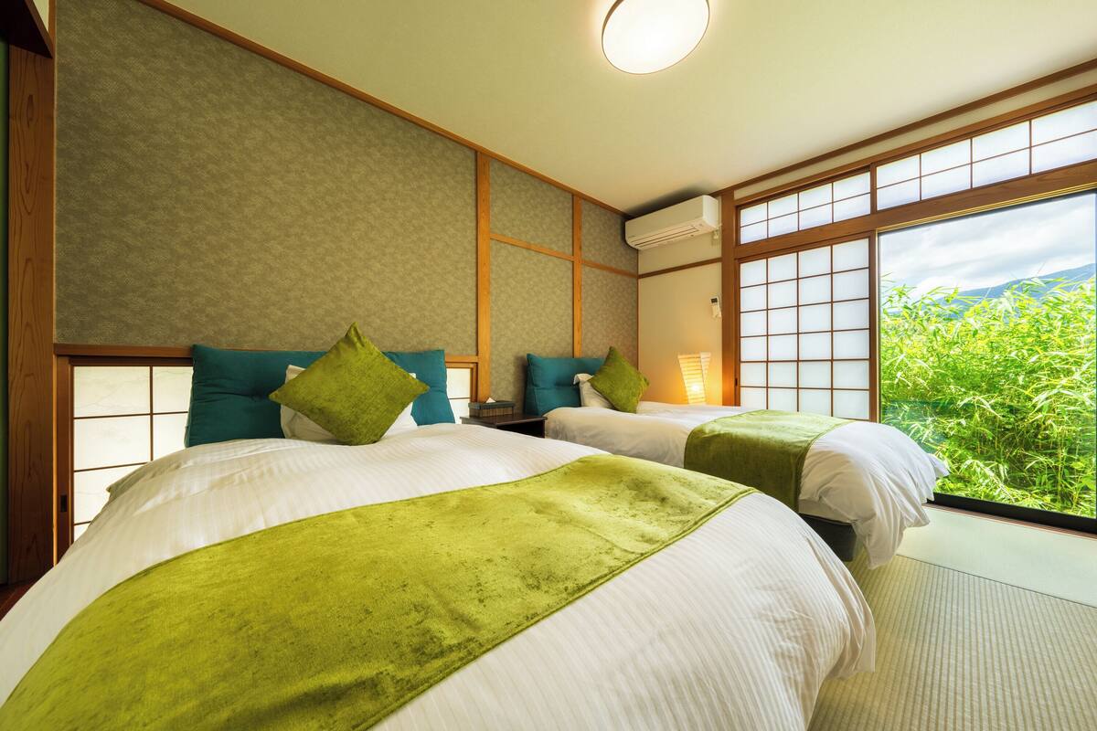 Une chambre d’hôtel avec deux lits, une grande fenêtre donnant sur un paysage verdoyant et un panneau mural de style traditionnel.