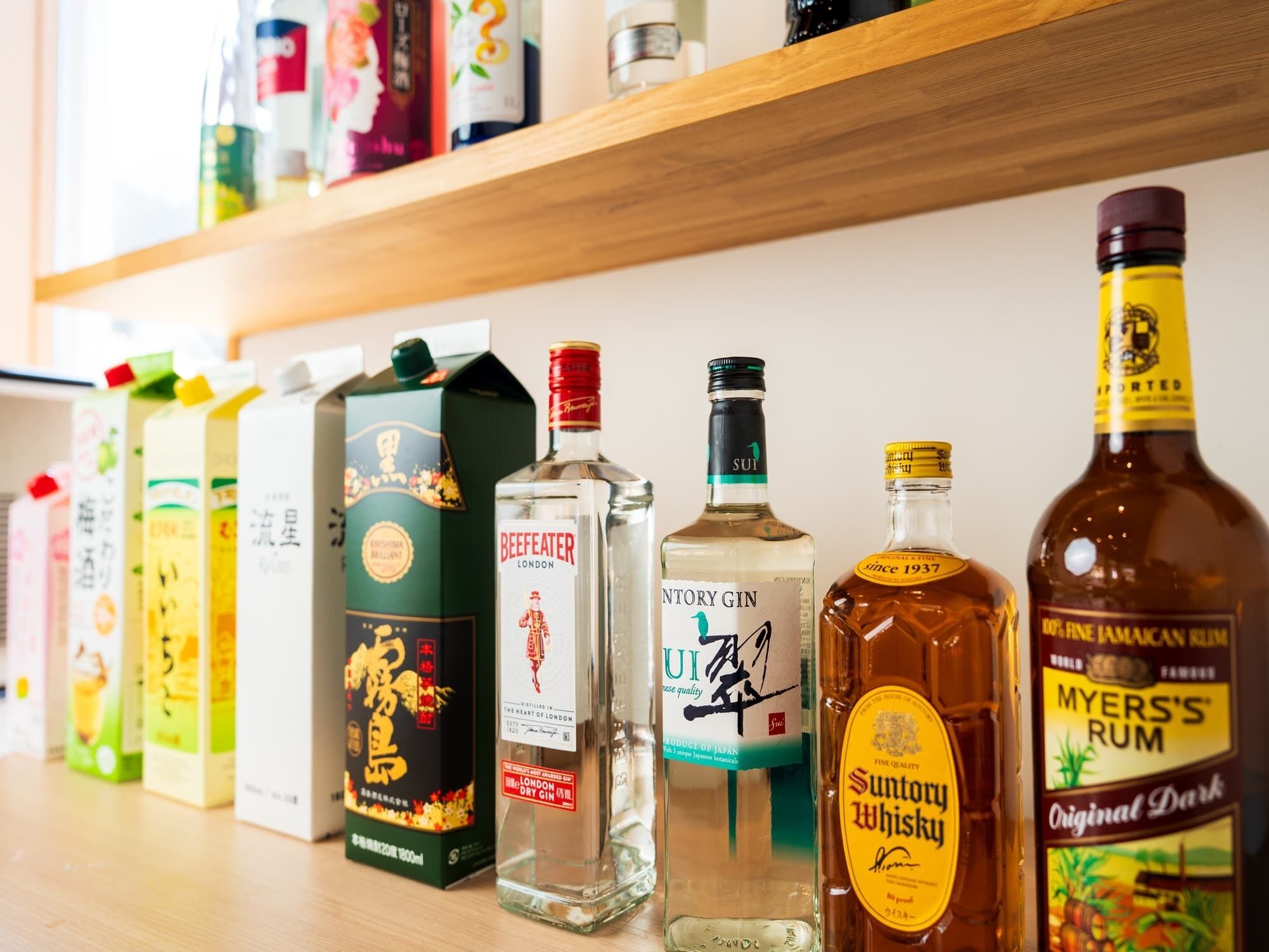 Variedad de bebidas alcohólicas en una estantería, incluyendo botellas y cartones.