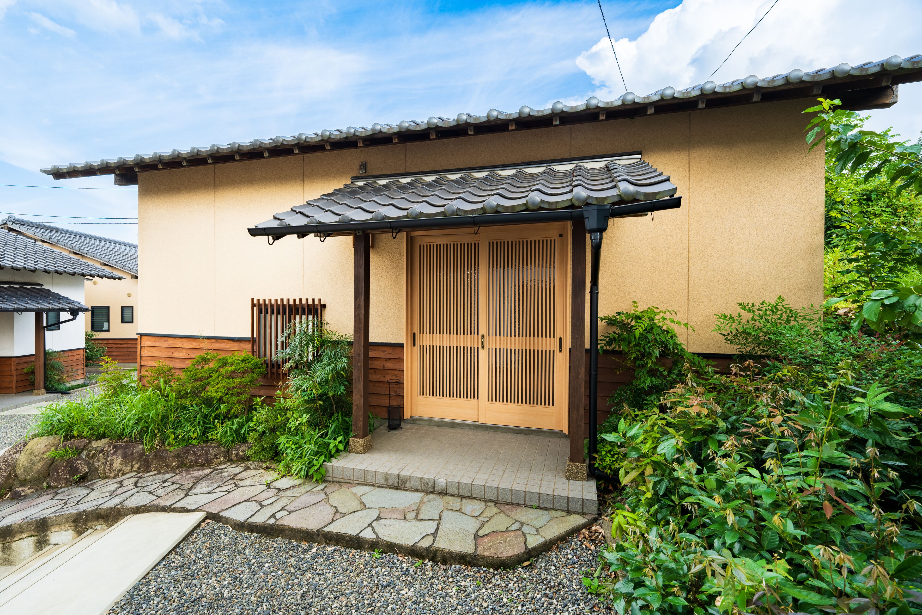 A traditional Japanese house with a tiled roof, wooden doors, and a stone pathway leading to the entrance.