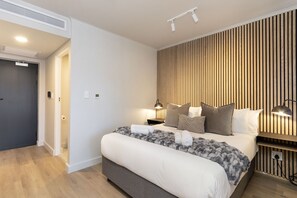 A modern bedroom with a large bed, bedside lamps, and a wooden slat wall. - The Tokyo Studio (Cape Town)