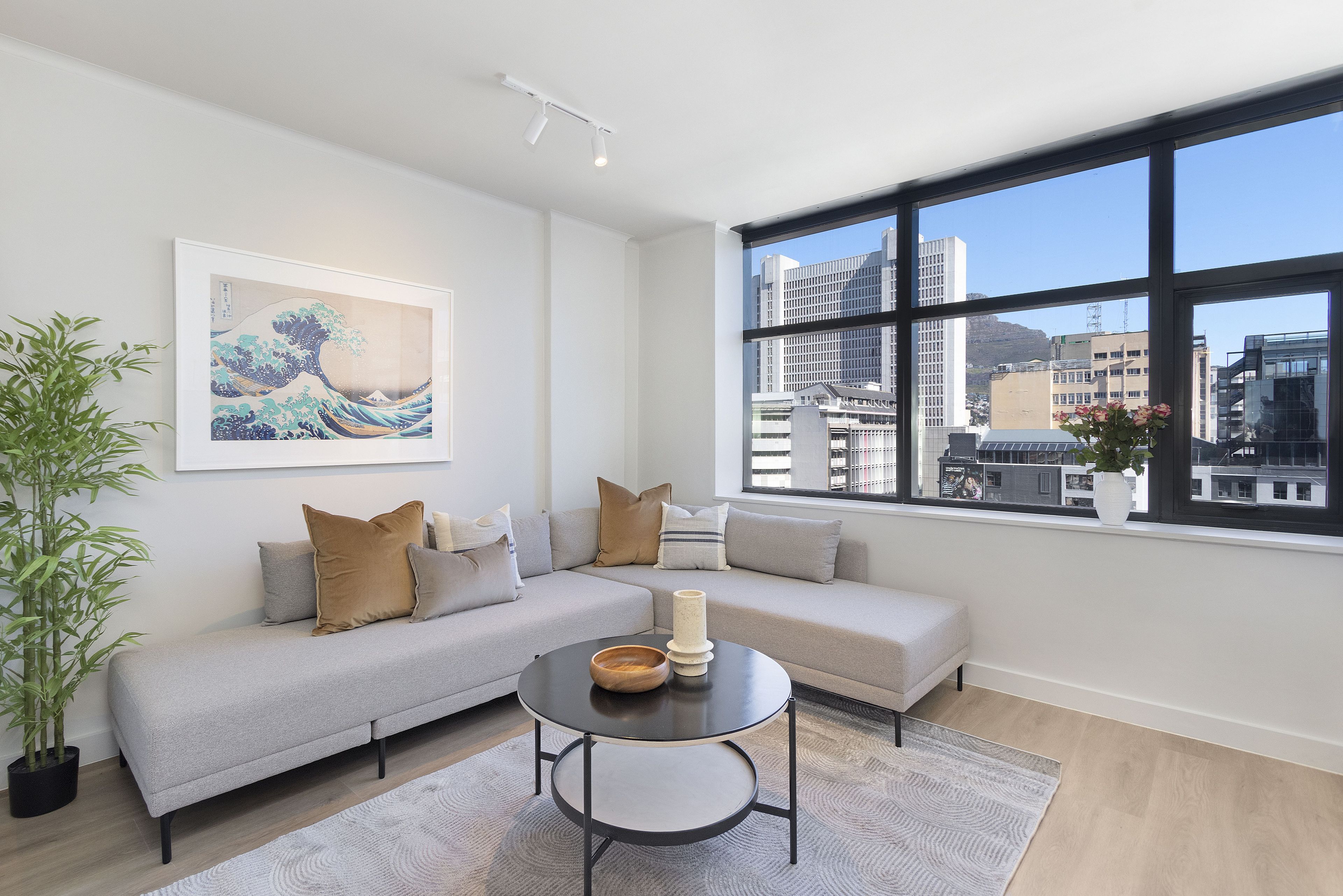 A modern living room with a grey sofa, a round coffee table, and a large window offering a city view.