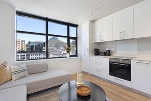 A modern kitchen with white cabinets, a black Bosch oven, and a large window offering a city view. - The Tokyo Studio (Cape Town)