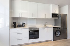 A modern kitchen with white cabinets, a Bosch oven, a microwave, a coffee maker, and a washing machine.