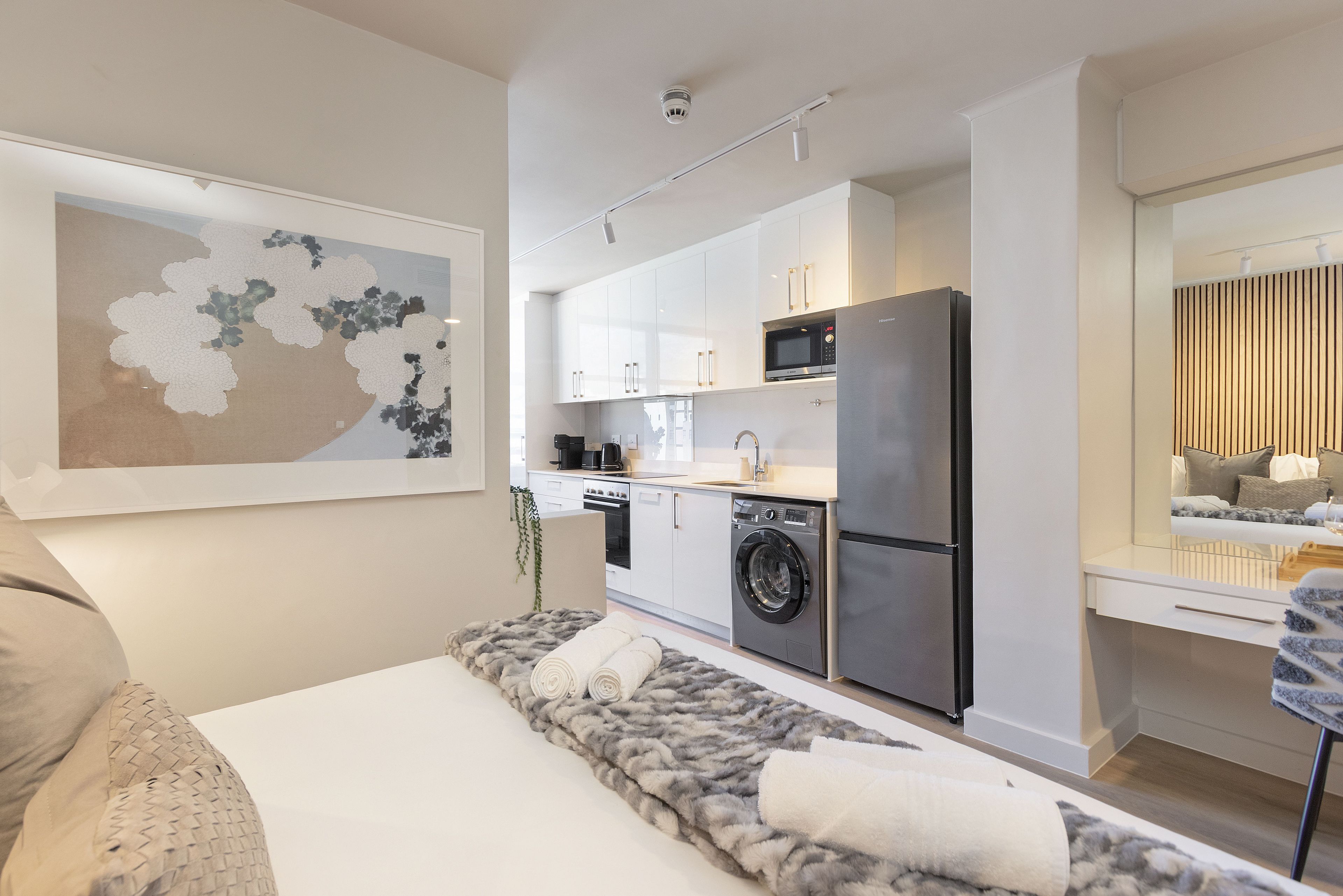 A modern apartment with a kitchenette, a bed with a fluffy rug, and a large framed artwork on the wall.