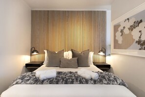 A modern hotel room with a large bed, a wooden slat headboard, two bedside lamps, and a framed artwork on the wall.