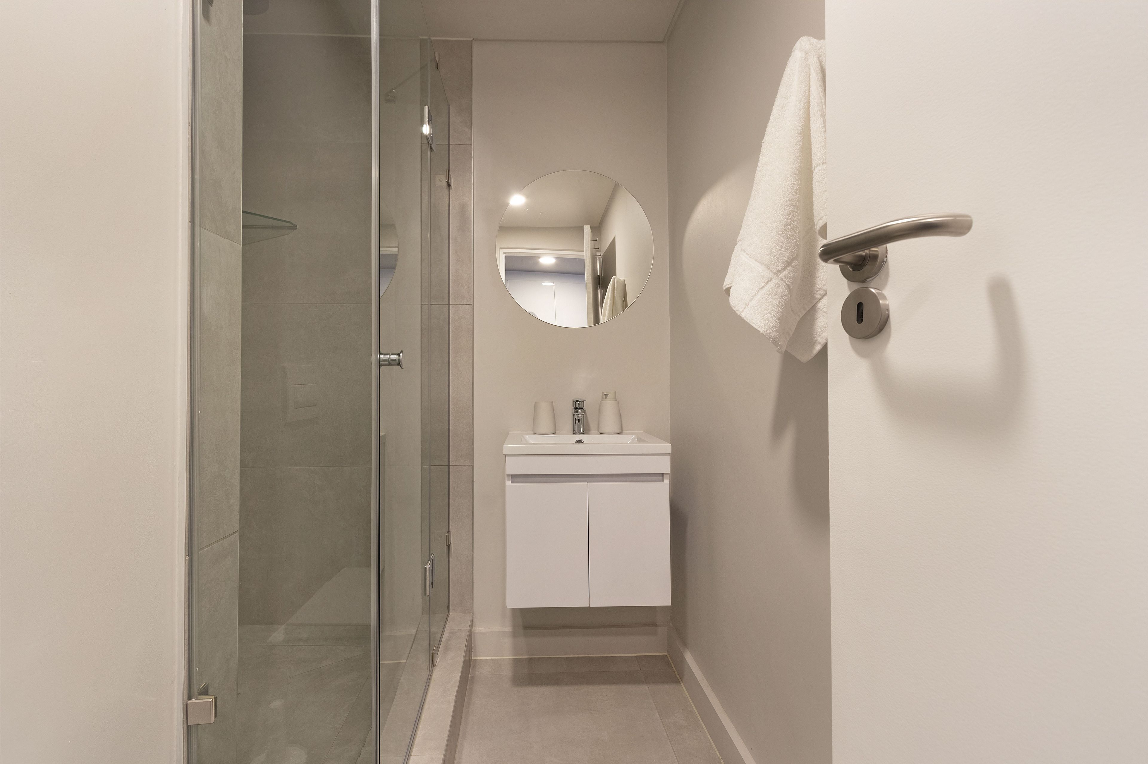 Un baño moderno con cabina de ducha de vidrio, un lavamanos blanco con espejo arriba y una toalla colgada en un perchero de metal.