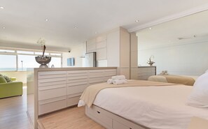 A modern bedroom with a large bed, a built-in wardrobe, and a view of the sea. - Sandringham 45 (Cape Town)