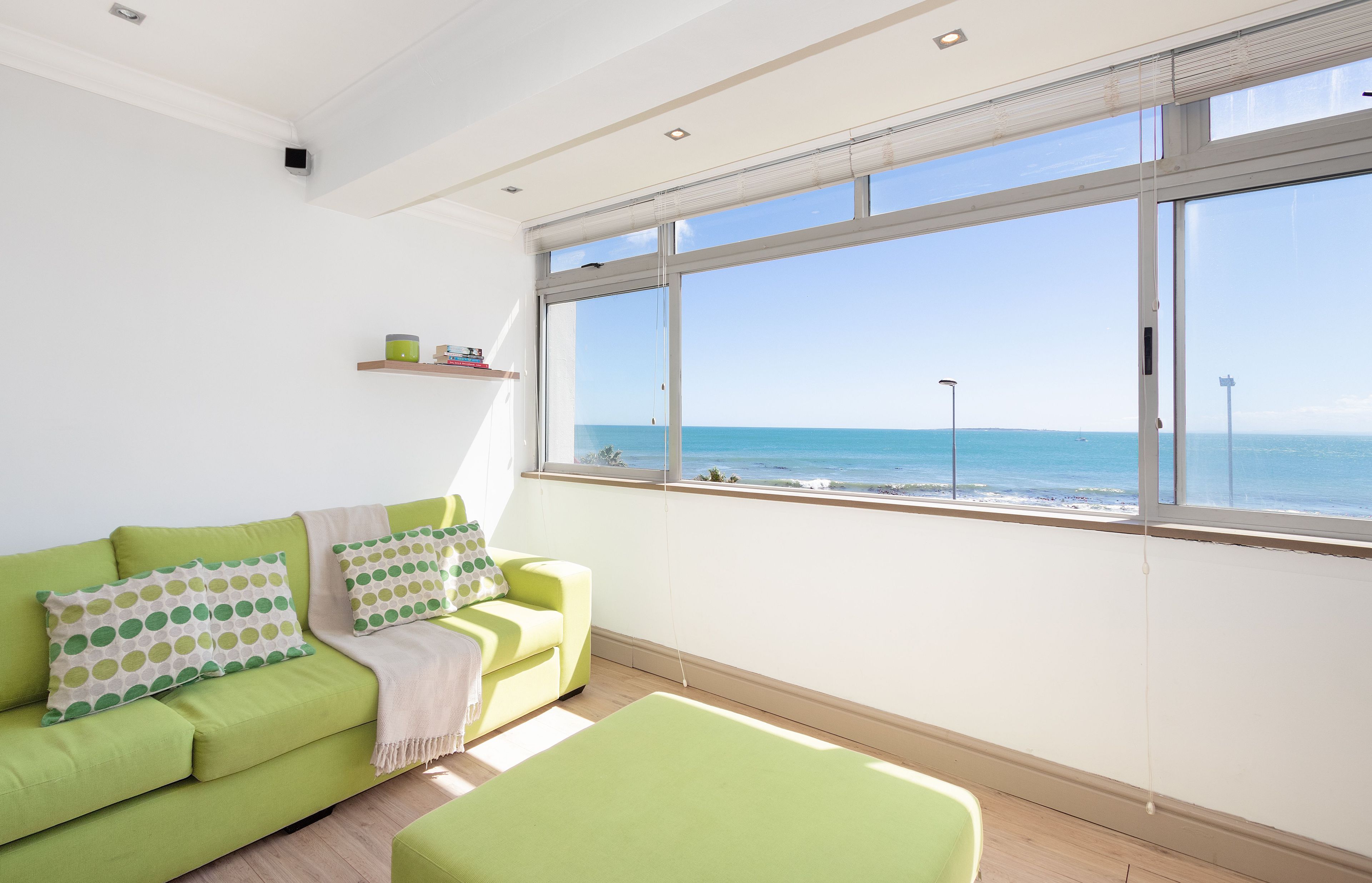 A bright room with a green sofa, a view of the sea, and a window with blinds.