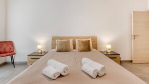 A neatly arranged hotel room with a large bed, two bedside tables, a red chair, and a wooden door.