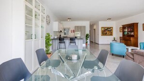 A modern living room with a glass dining table, a kitchen in the background, and a blue armchair.
