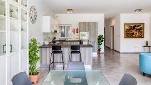 A modern kitchen with a central island, bar stools, and a dining area with a glass table.
