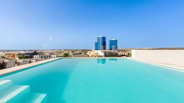 Ein Dachpool mit klarem, blauem Wasser, umgeben von modernen Gebäuden und blauem Himmel.