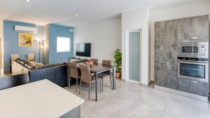 Ein modernes Wohnzimmer mit Essbereich, einer Couch, einem Fernseher und einer Küche mit Einbaugeräten.
