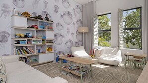 A modern living room with a white sofa, a wooden coffee table, and a bookshelf filled with children's toys and books. - Hout Bay Villa (Cape Town)