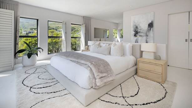 A modern bedroom with a large bed, a bedside table, a nightstand, and a large window offering a view of greenery. - Hout Bay Villa (Cape Town)