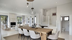 A spacious living area with a large wooden dining table, white chairs, and a modern chandelier. - Hout Bay Villa (Cape Town)