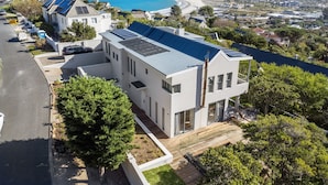 A modern two-story building with solar panels, surrounded by lush greenery and a coastal view. - Hout Bay Villa (Cape Town)