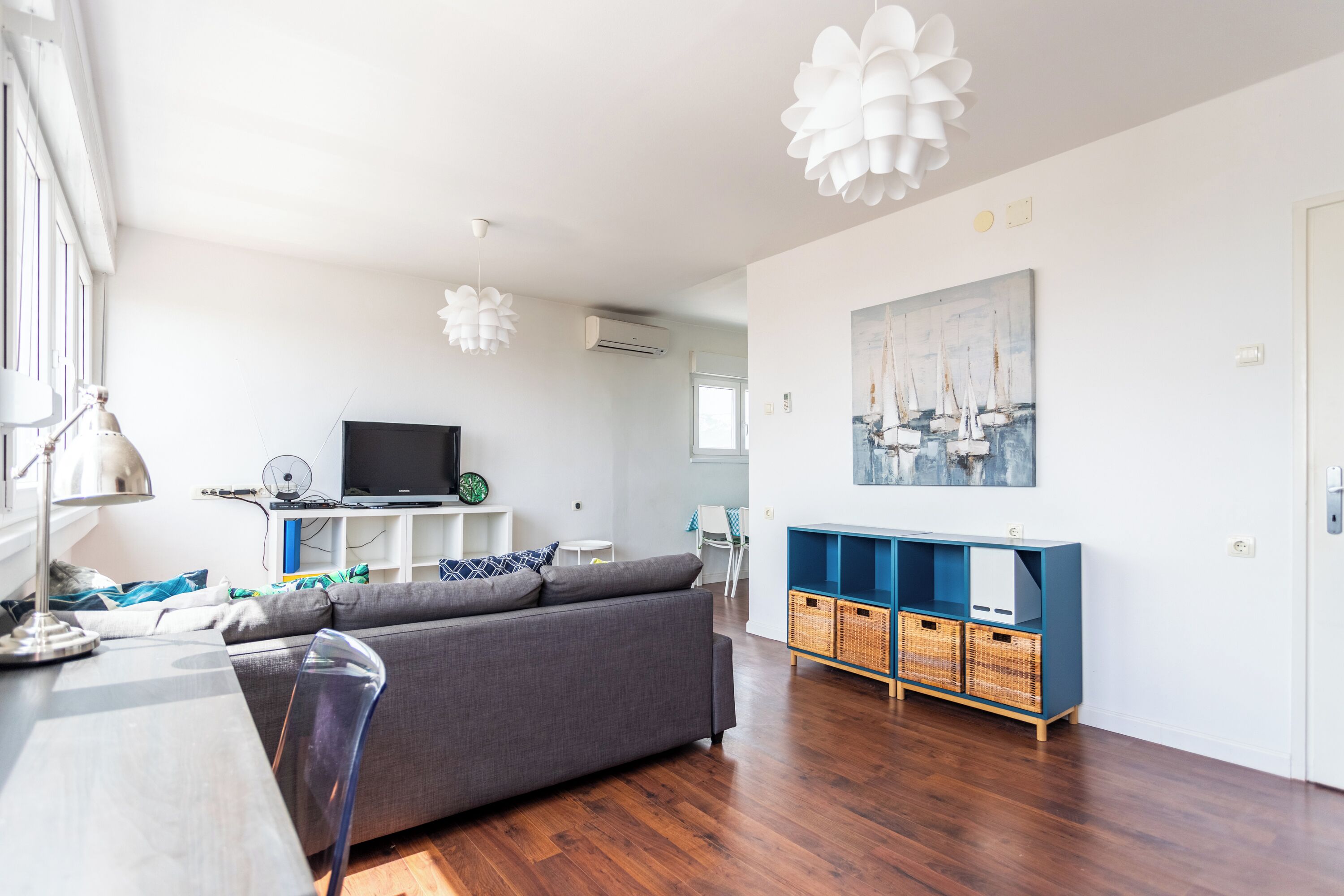 A modern living room with a grey sofa, wooden flooring, a TV, and a blue entertainment unit.