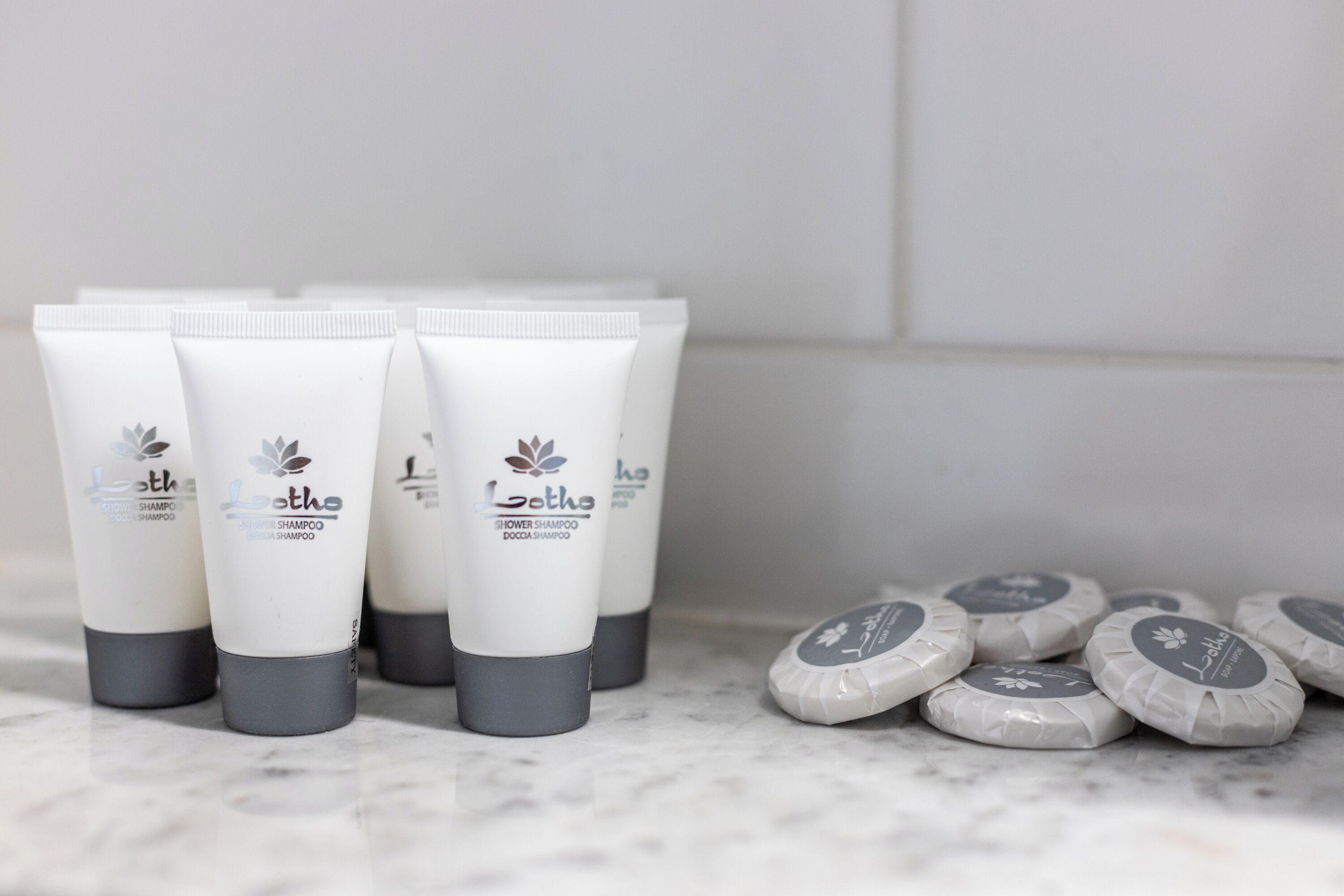 Un ensemble de tubes de shampoing pour la douche, de couleur blanche, avec des bouchons gris, posés sur une surface en marbre.