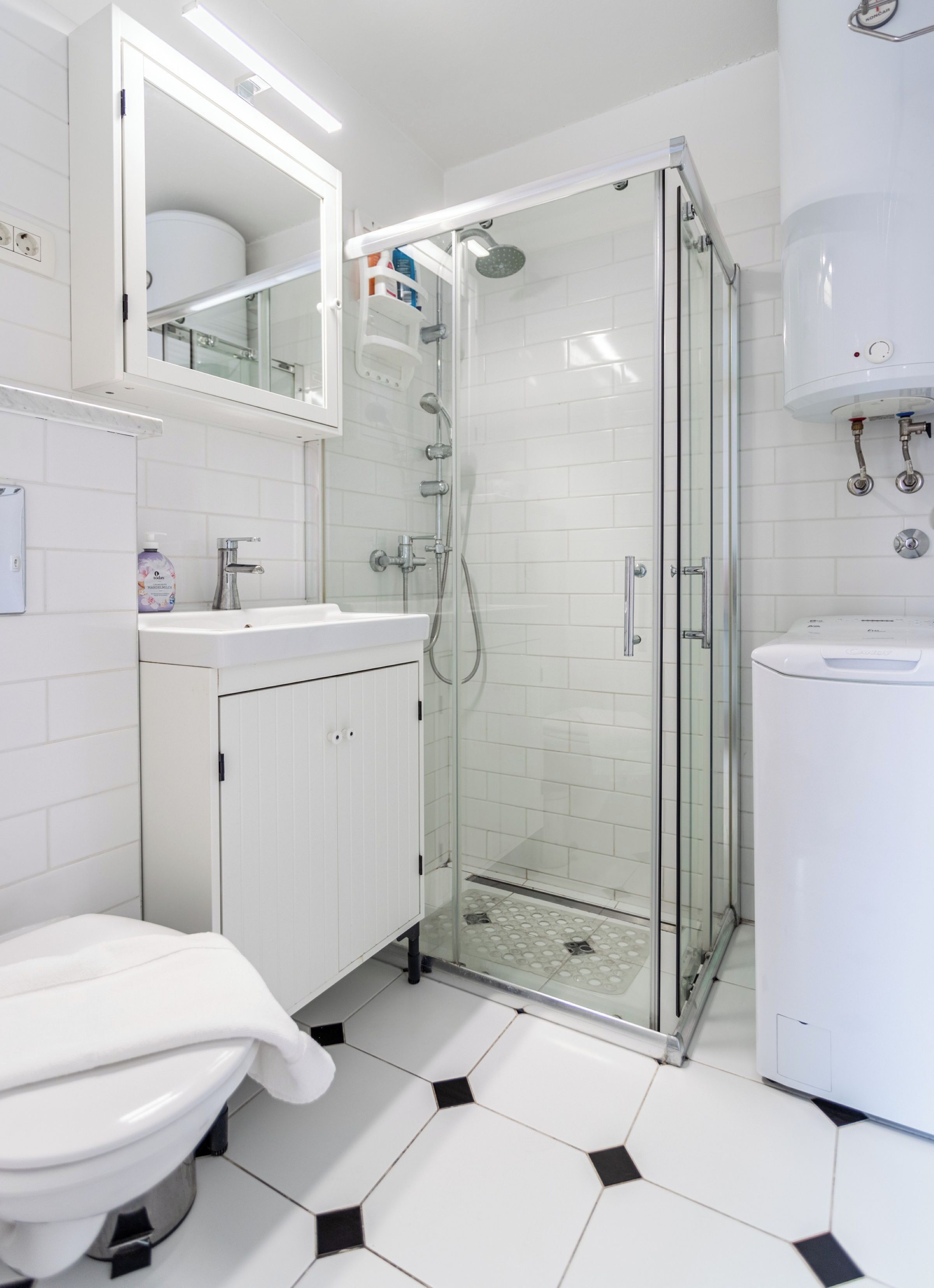 A modern bathroom with a glass-enclosed shower, white tiles, a white sink, and a toilet.