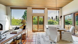 A spacious living area with a wooden ceiling, large windows offering a view of greenery, a dining table with chairs, and a fireplace. - Red Rock Views: Uptown Sedona Home Near Trails! (Sedona)