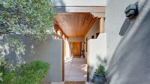 A covered walkway leading to a wooden door, surrounded by a stucco wall and a potted plant. - Red Rock Views: Uptown Sedona Home Near Trails! (Sedona)