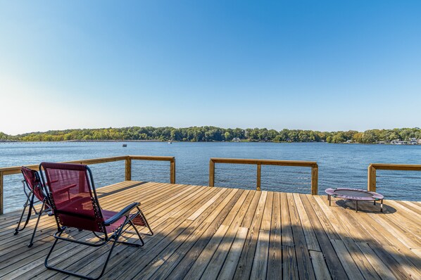 A wooden deck with a view of a lake, a trampoline, and a red chair. - Monticello Vacation Rental w/ Private Boat Dock! (Monticello)