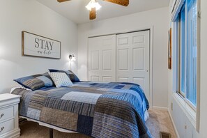 Un dormitorio con cama, mesita de noche, lámpara de pared, puerta y ventana con persianas.