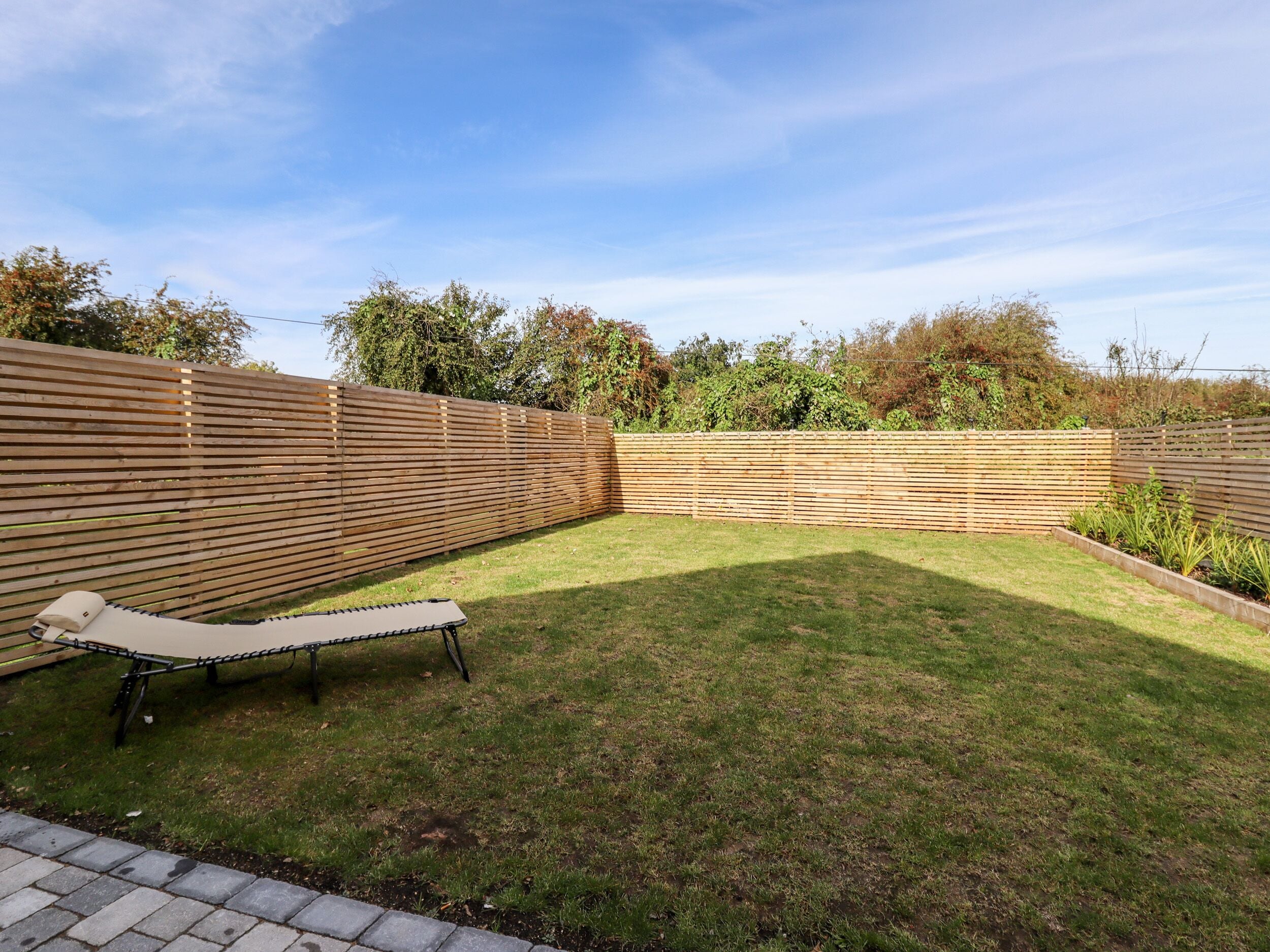 Un jardin avec une clôture en bois, une pelouse verdoyante et un fauteuil de jardin.