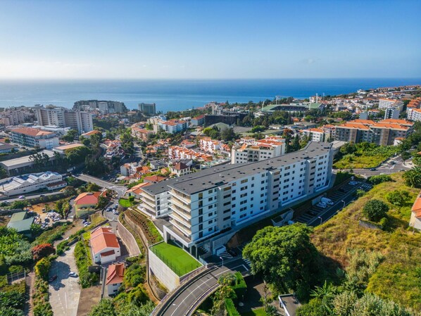 Un immeuble de grande hauteur, doté de nombreux étages, entouré de verdure et offrant une vue sur la côte.
