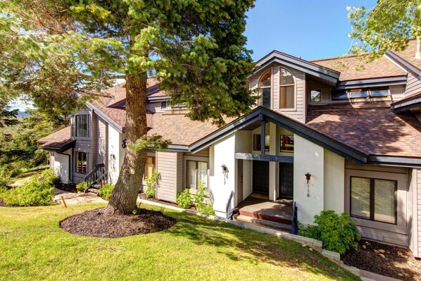 A two-story house with a large tree in the front yard, a covered porch, and a garage.