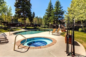 A swimming pool with a circular hot tub, surrounded by lounge chairs and a fence.
