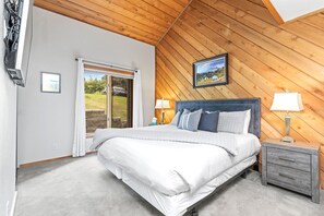 A bedroom with a bed, a nightstand, a lamp, a picture on the wall, and a sliding door to the outside.