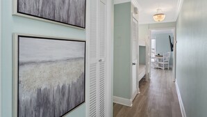 A hallway with light green walls, white doors, and a chandelier. There are framed artworks on the walls and a dining area in the background. - Summer Breeze 1-Bed Condo! Gorgeous Views & Pool | Steps to Beach | Book Now! (Miramar Beach)