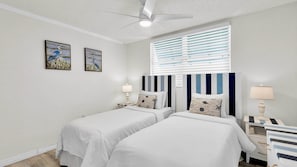 Une chambre d’hôtel avec deux lits, un ventilateur de plafond, une fenêtre avec des stores et des œuvres d’art accrochées au mur.
