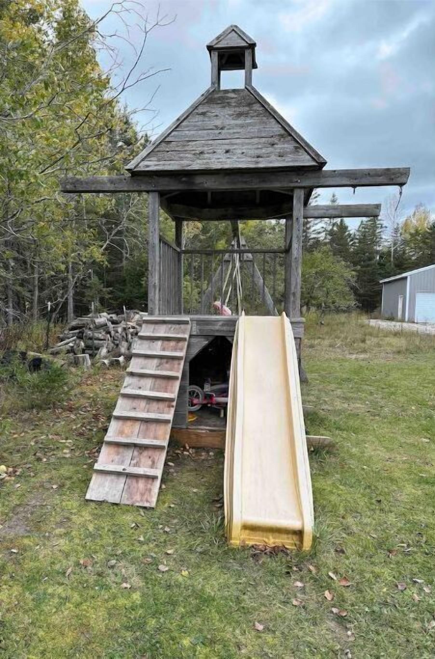 A wooden play structure with a slide and a small shelter.