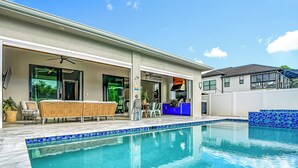 A modern house with a swimming pool, outdoor seating, and a kitchen area. - Luxurious 2023 New Construction — Executive Vacation Home Near Vanderbilt Beach (Naples)