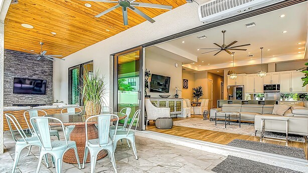 A modern living room with a dining area, wooden ceiling, and a large TV mounted on the wall. - Luxurious 2023 New Construction — Executive Vacation Home Near Vanderbilt Beach (Naples)