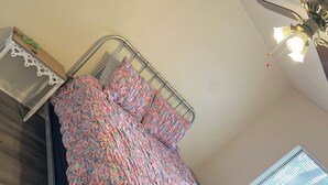 A bed with a metal frame and a floral bedspread, a ceiling fan, and a window with blinds. - Amazing 3 Bedroom Across From UF
 (Gainesville)