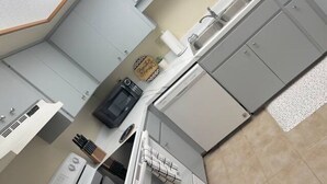 A compact kitchen with white cabinets, a built-in oven, a coffee machine, and a small sink. - Amazing 3 Bedroom Across From UF
 (Gainesville)