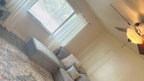 A room with a large window, a ceiling fan, and a patterned rug. - Amazing 3 Bedroom Across From UF
 (Gainesville)