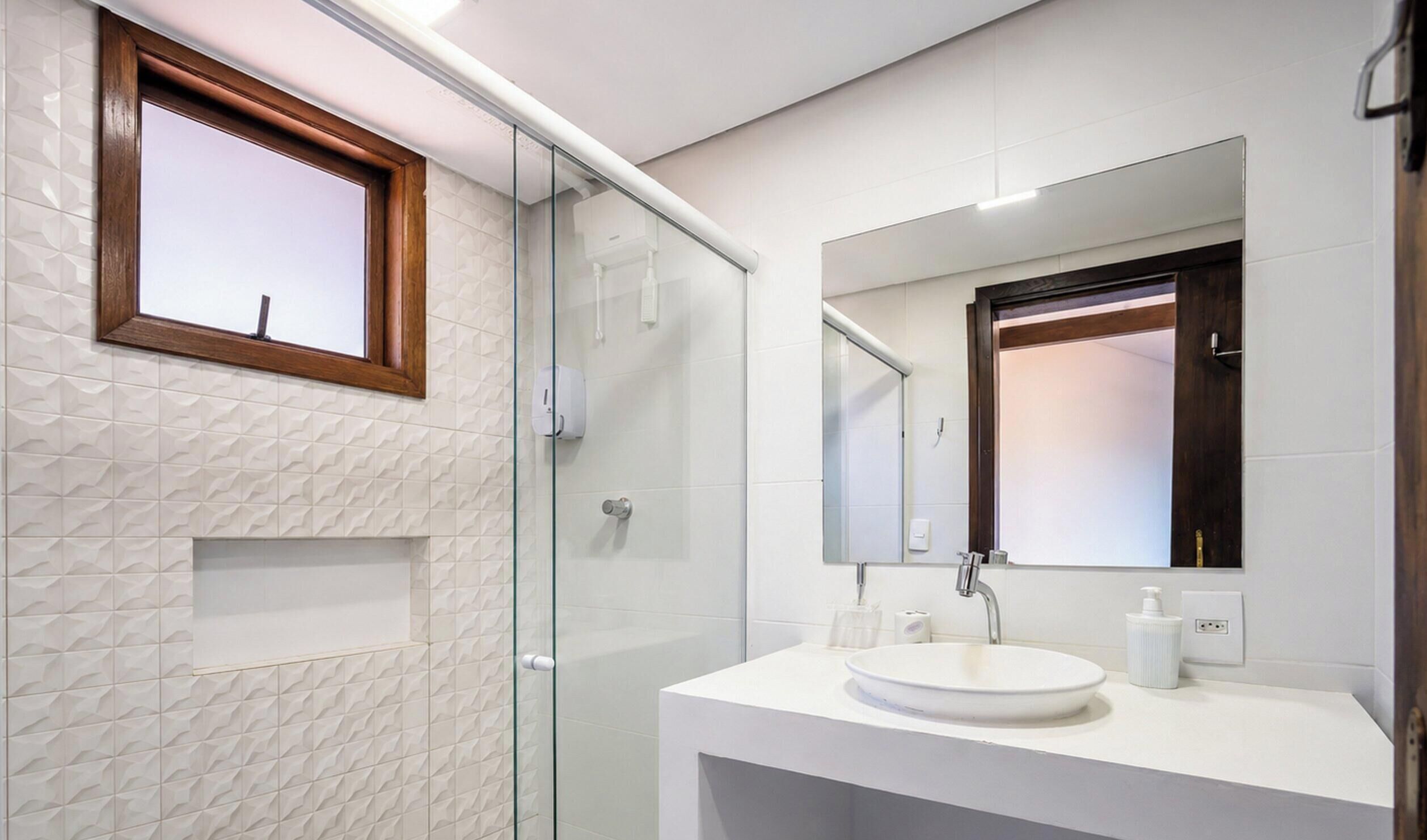 Un baño moderno con cabina de ducha de vidrio, un lavabo blanco y un espejo grande.